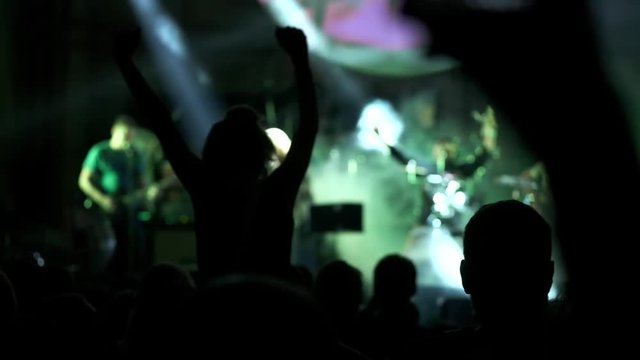Shot of some cheering fans at a life concert, slow motion. girl at a concert seating on shoulders and raising her hands.