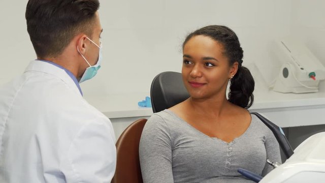 Young beautiful African American woman smiling joyfully, talking to the dentist. Attractive female patient visiting her dentist. Communication, medical service, dentistry concept.