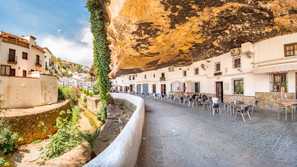 Restaurants in houses built in caves into rock overhangs above the Rio Trejo in the white village of Setenil de las Bodegas, Spain. - obrazy, fototapety, plakaty