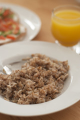 Oat meal porridge breakfast in white plate dish with spoon. Eating breakfast morning. Wooden table. Close up healthy food.