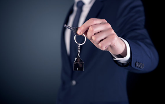 Young businessman hand over keys with empty dark background
