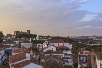 Fototapeta premium View of narrow streets and castle of Obidos from wall of fortress. Scenic old town with medieval architecture in the sunset. White houses red tiled roofs.
