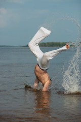 Person practicing capoeira on the beach is a concept of people, lifestyle and sports. Man doing battle in the water