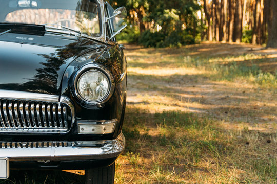 half of a black, old, vintage car with glare from the sun, which stands on a clearing in the valley on a summer day.