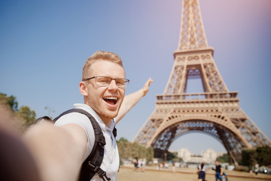 Man tourist with backpack and wearing glasses makes selfie photo on background of Eiffel Tower in Paris, France. Concept travel.