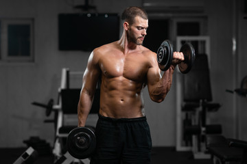 Fototapeta na wymiar Man trains in the gym. Athletic man trains with dumbbells, pumping his biceps