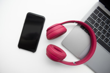 Flay lay of pink headphone, smartphone and laptop on white screen