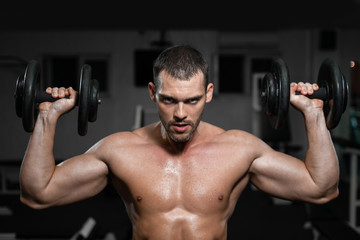 Fototapeta na wymiar Muscular man in the gym training with dumbbells, guy pumps his deltoid muscle