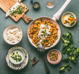 Healthy vegetarian couscous pot with ingredients bowls: vegetables, herbs and feta cheese on dark background, top view, flat lay.