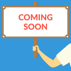 COMING SOON. Hand holding wooden sign
