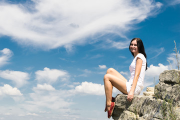 Obraz na płótnie Canvas girl with black hair, in white clothes and red shoes, sits at the edge of the rock