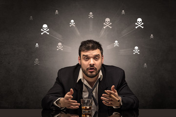 Loser drunk man sitting at table with skulls concept around
