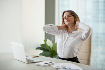 Exhausted millennial businesswoman stretch in chair, massaging neck after long working hours, tired...