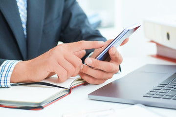 Businessman in black suit using mobile smart phone and working on laptop computer close up. Just hands handss over the table.