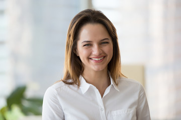 Portrait of happy millennial female office worker posing for picture at workplace, successful businesswoman smiling looking at camera, confident employee shooting for company advertising or catalogue