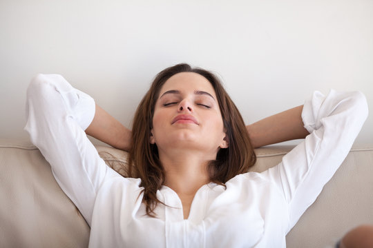 Relaxed woman lying eyes closed hands over head on cozy sofa at home, calm millennial female sleeping or taking nap during lazy morning, spending weekend in apartment, girl chilling or taking break