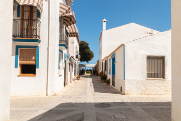 Narrow, stone street with bright, old houses on both sides. The buildings have nienieskie and colorful shutters in the windows. Tabarca, Spain, Europe. A beautiful, summer, sunny day.