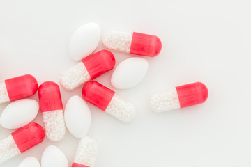 White pills and red-white capsules on a white background, place for text.
