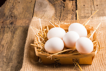 Chicken eggs in the basket with straw on the wooden table