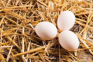 Three chicken eggs on the straw and on the wooden table