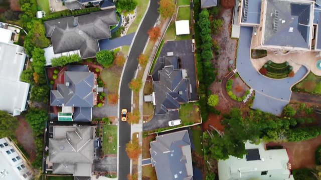birds eye view of Orange Lamborghini driving down winding suburban street slow motion aerial drone