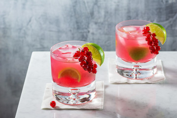 Two Cold Red Currant Caipirinha or Daiquiri Cocktails with Lime Wedges in Glasses on Marble Bar Counter