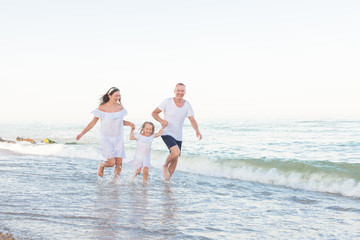 Parents with a daughter running along the seashore.