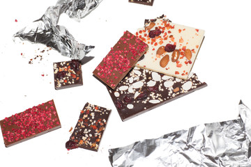 different pieces of chocolate with topping in foil isolated on white background