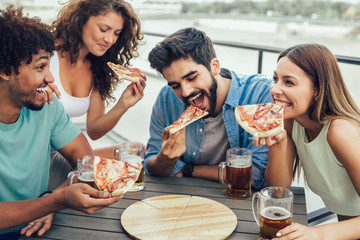Friends enjoying pizza. Group of young cheerful people eating pizza and drinking beer while sitting...