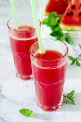 Cold watermelon lemonade with mint in a glass cup and slices of watermelon on a light background.