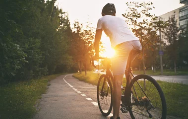 Foto op Plexiglas Fietsen De jonge man in vrijetijdskleding fietst op de weg in de avondstad