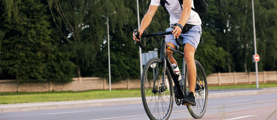 The young guy in casual clothes is cycling on the road in the evening city