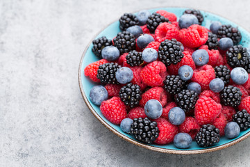 Fresh berry salad on blue dishes. Vintage wooden background.