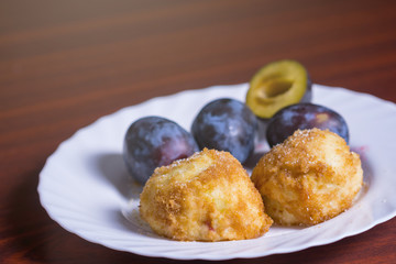 Fresh plum dumplings. Two dumplings with fresh plums on white plate on dark red table