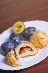 Fresh plum dumplings. One sliced dumpling and one whole with fresh plums on white plate on dark red table