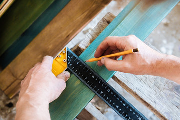 the man master marks with a pencil and a measuring ruler a place for the cut of the Board. Wooden Board lining is painted with bright color paint. Repair workshop.