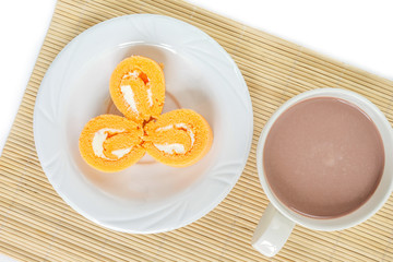 orange cake roll three piece on white plate and cup chocolate on wooden mat.
