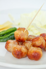 Grilled sausage ball on a white plate on white background.