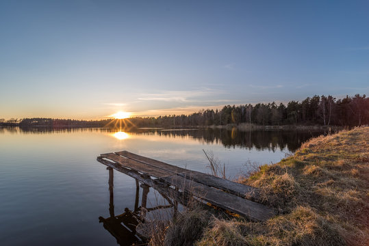 Reflections of the sunset on a pond with a small wooden boat bridge