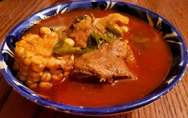 Porcelain plate with blue details with mole de olla, typical Mexican soup with various ingredients such as corncob, pork, chile ancho and guajillo chili on a wooden table
