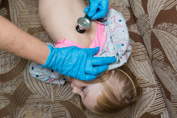 A pediatrician doctor examines the back of a sick girl using a phonostage. Home visit.