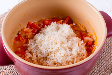 Raw rice with vegetables in a pan on wooden background