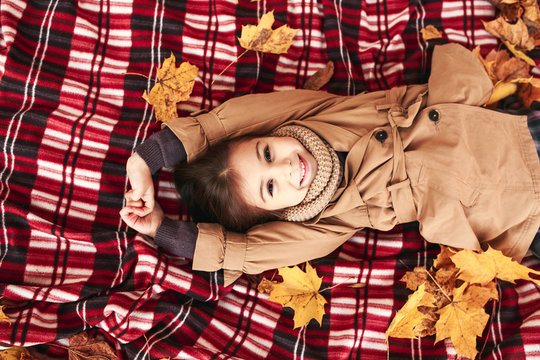 Little girl lying in maple leafs in park
