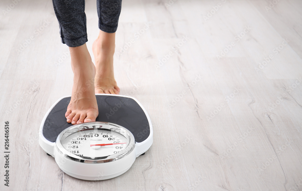 Wall mural Woman measuring her weight using scales on floor