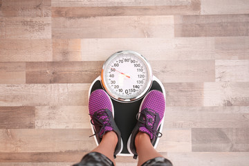 Woman measuring her weight using scales on floor, top view