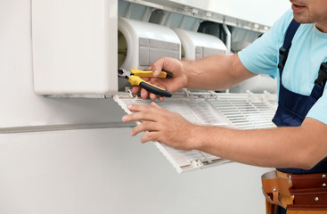 Male technician repairing modern air conditioner indoors