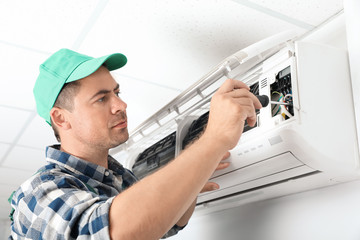 Naklejka na ściany i meble Male technician repairing air conditioner indoors