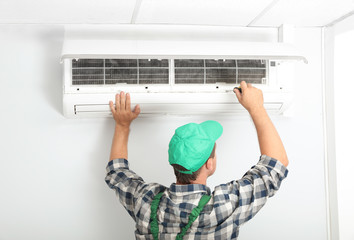 Male technician fixing modern air conditioner indoors