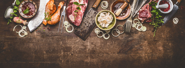 Various grill an bbq meats on rustic wooden background with aged kitchen and butcher tools, herbs,...