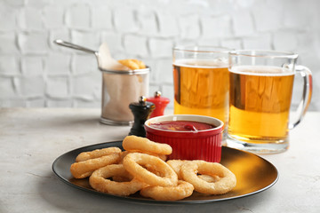 Plate with onion rings and bowl of sauce on table